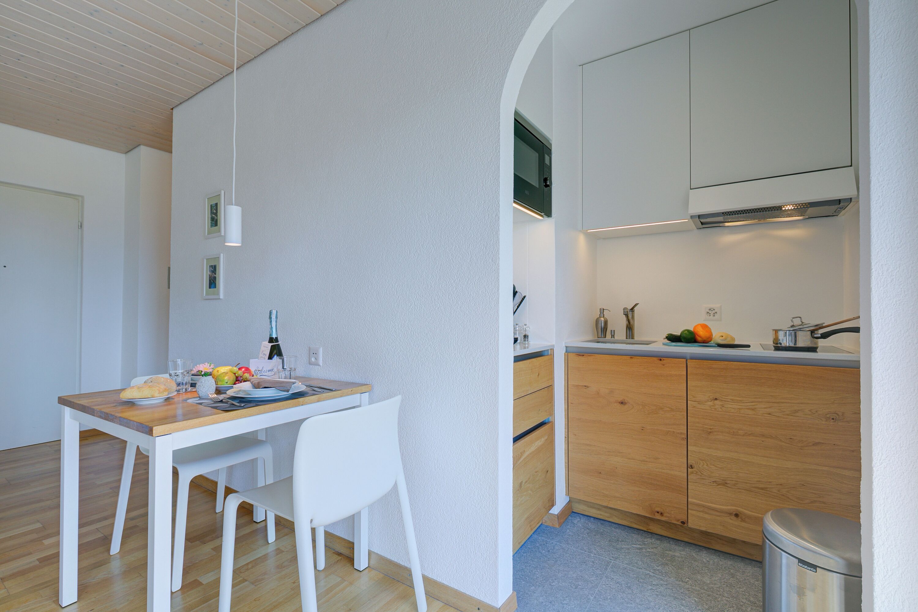 Una cocina moderna con armarios de madera, encimera blanca y un comedor con mesa de madera y sillas blancas.