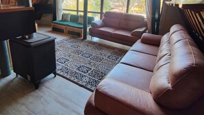 A cozy loft-style room with a large window, a sofa, a small table, and a rug. - Blackbird Cottage Bhimtal (Tallital Bhimtal)
