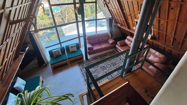 A room with a sloped ceiling, large windows, a sofa, and a patterned rug. - Blackbird Cottage Bhimtal (Tallital Bhimtal)