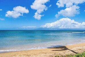 Una playa con agua azul cristalina, una orilla arenosa y una montaña al fondo.