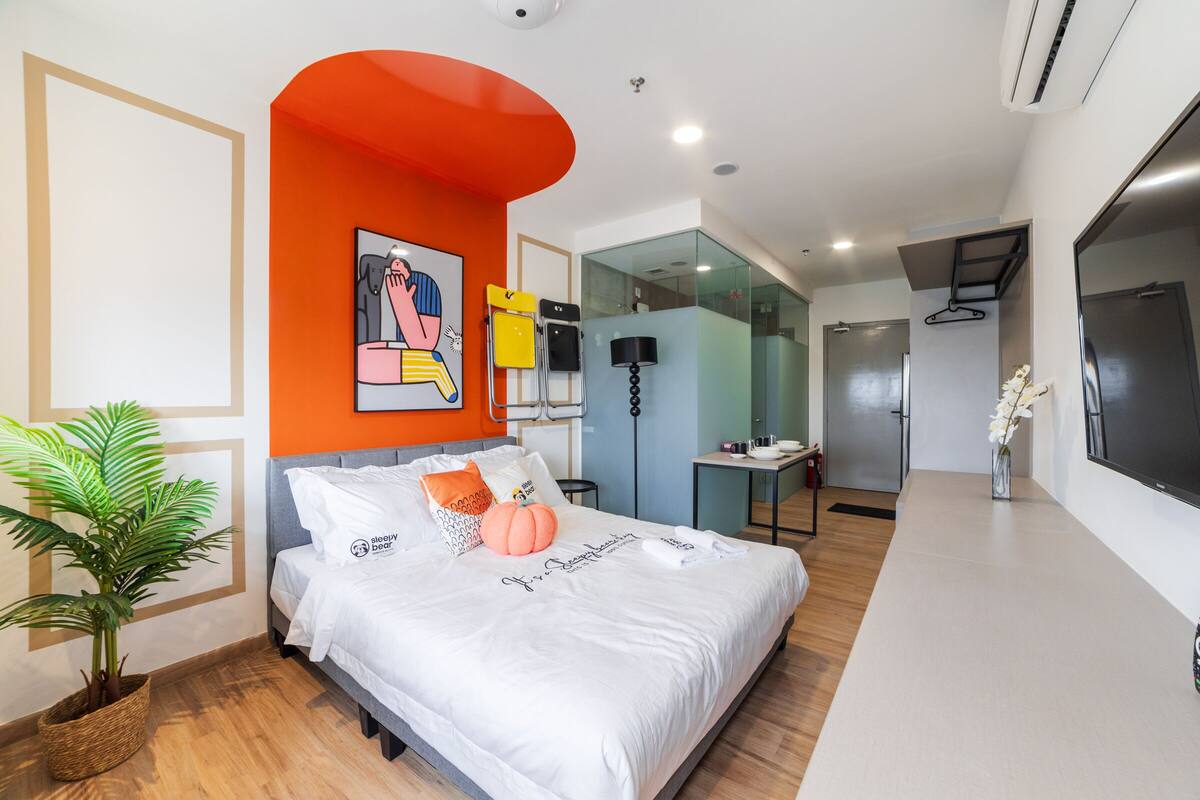 Ein modernes Hotelzimmer mit einem großen Bett, einer Zimmerpflanze, einem Gemälde und Blick ins Badezimmer.