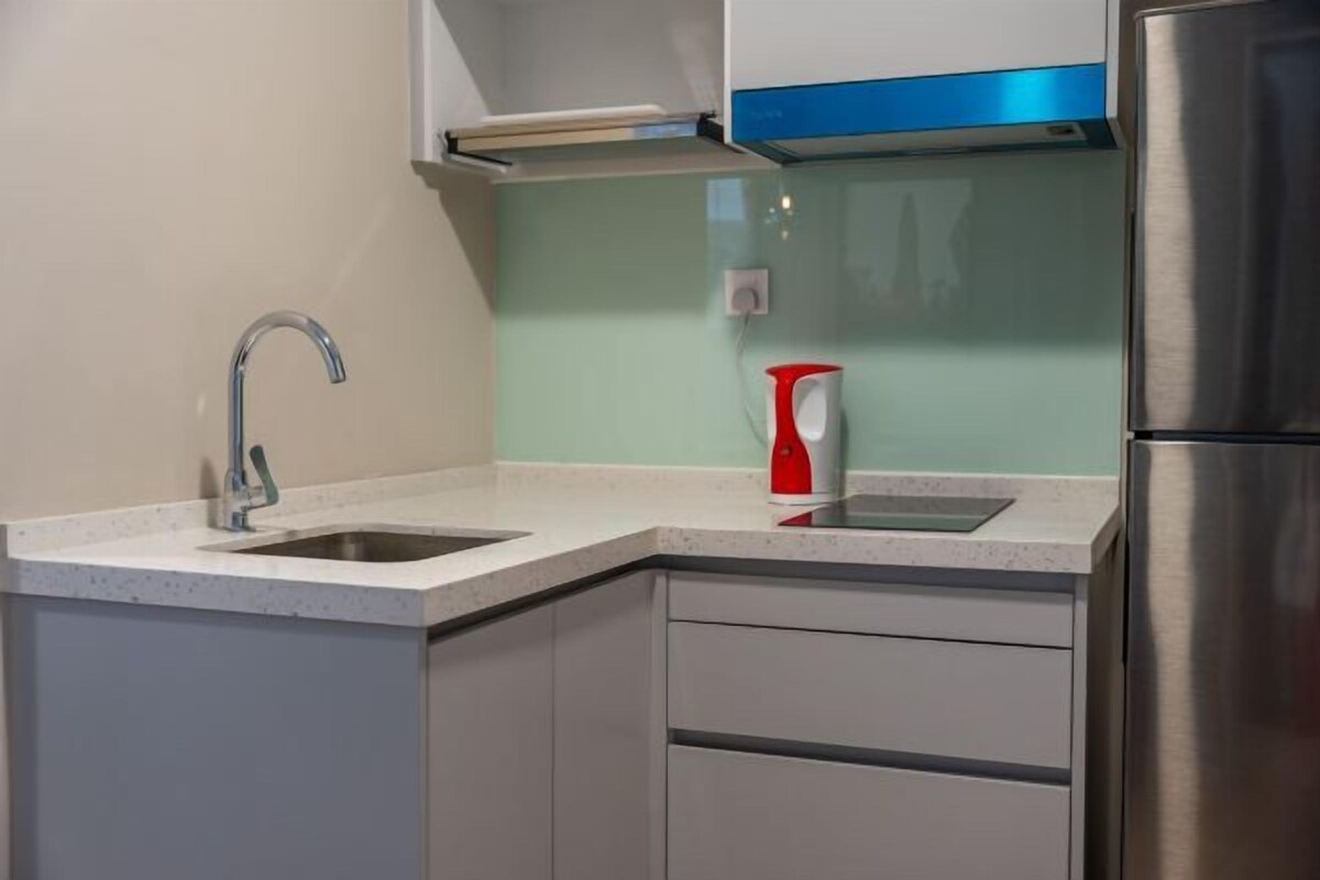 A kitchen with a stainless steel refrigerator, a sink with a modern faucet, and a red kettle on the countertop.