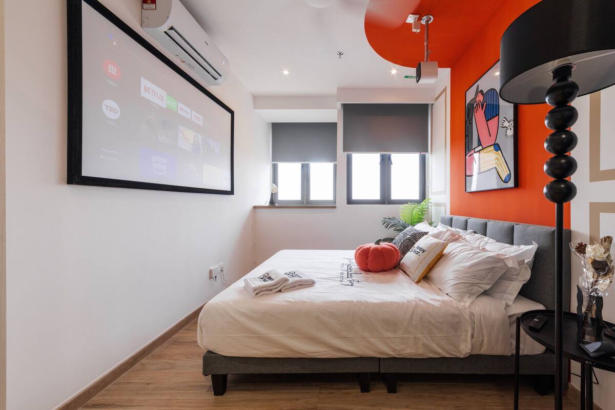 Ein modernes Schlafzimmer mit einem Bett, einem an der Wand montierten Projektor und einem großen Fenster.
