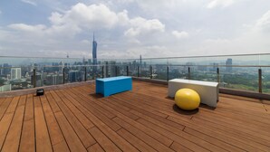 A rooftop terrace with a wooden deck, two exercise balls, and a blue and white bench. A city skyline with a prominent tower is visible in the background. - Riveria City KL Sentral by Sleepy Bear (Kuala Lumpur)