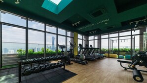 A gym with exercise equipment, large windows, and a view of a city skyline. - Riveria City KL Sentral by Sleepy Bear (Kuala Lumpur)