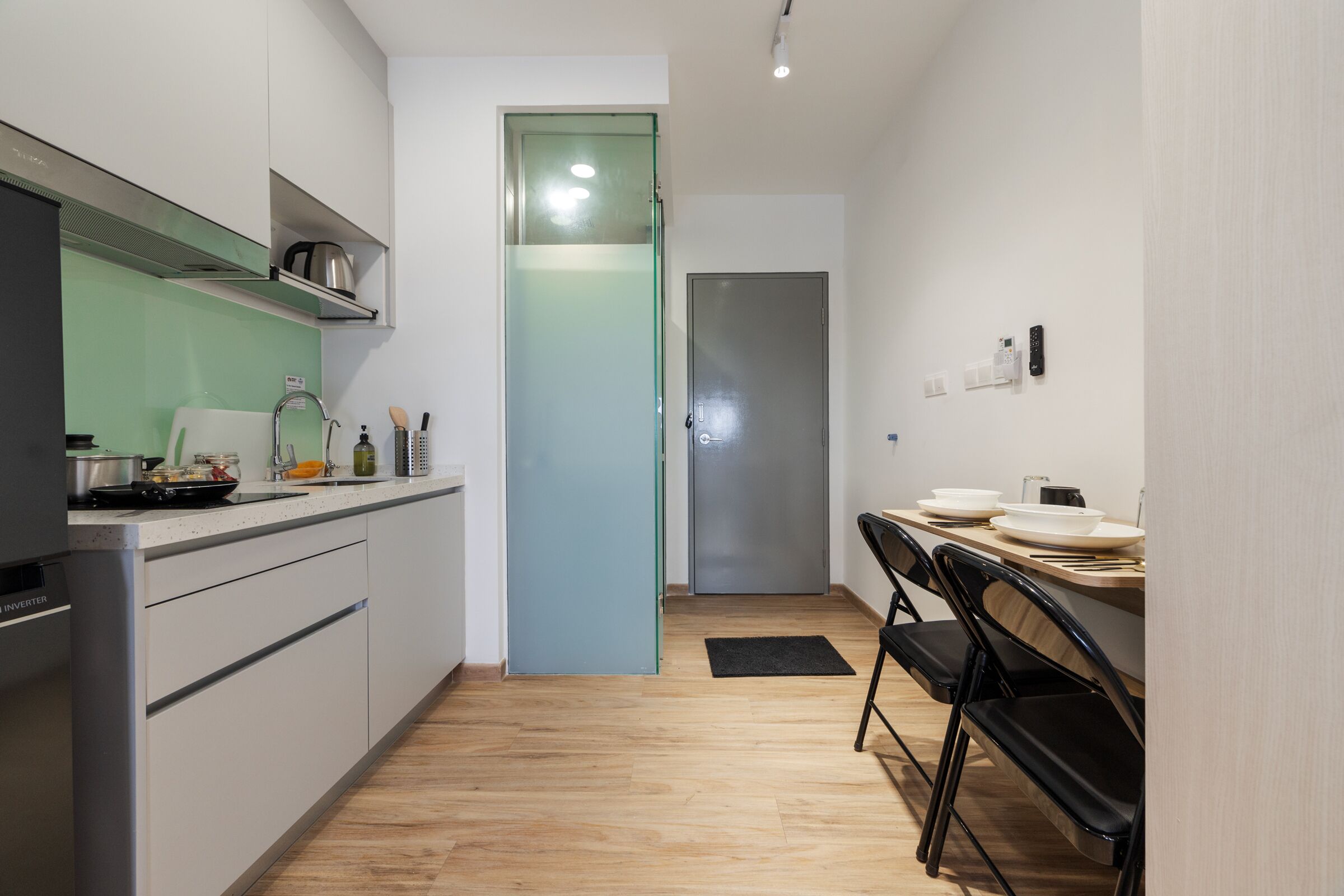 A modern kitchen with white cabinets, a stainless steel refrigerator, and a glass door leading to a hallway.