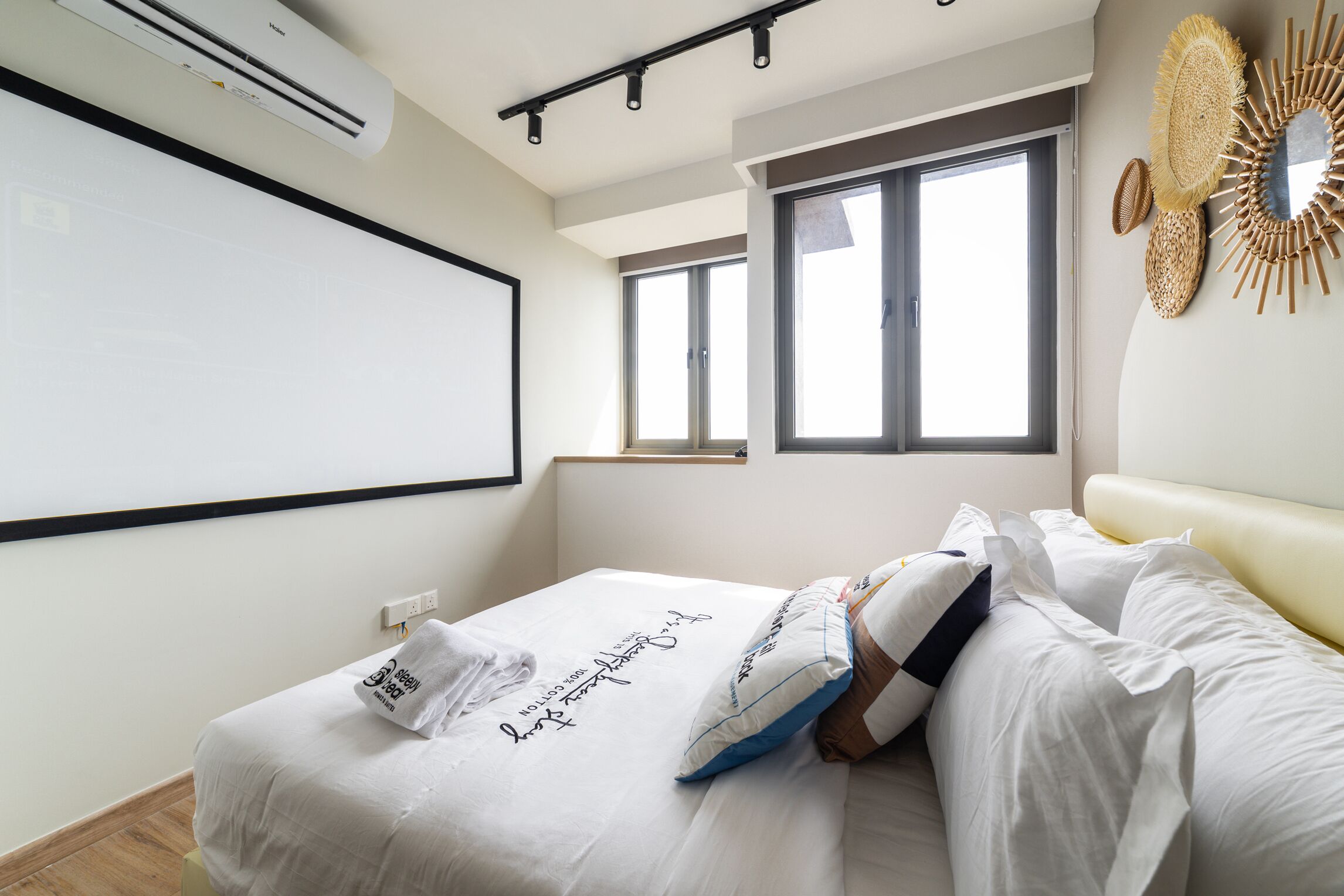 Un dormitorio moderno con una cama grande, un aire acondicionado de pared, una pantalla de proyector y una ventana con persianas.