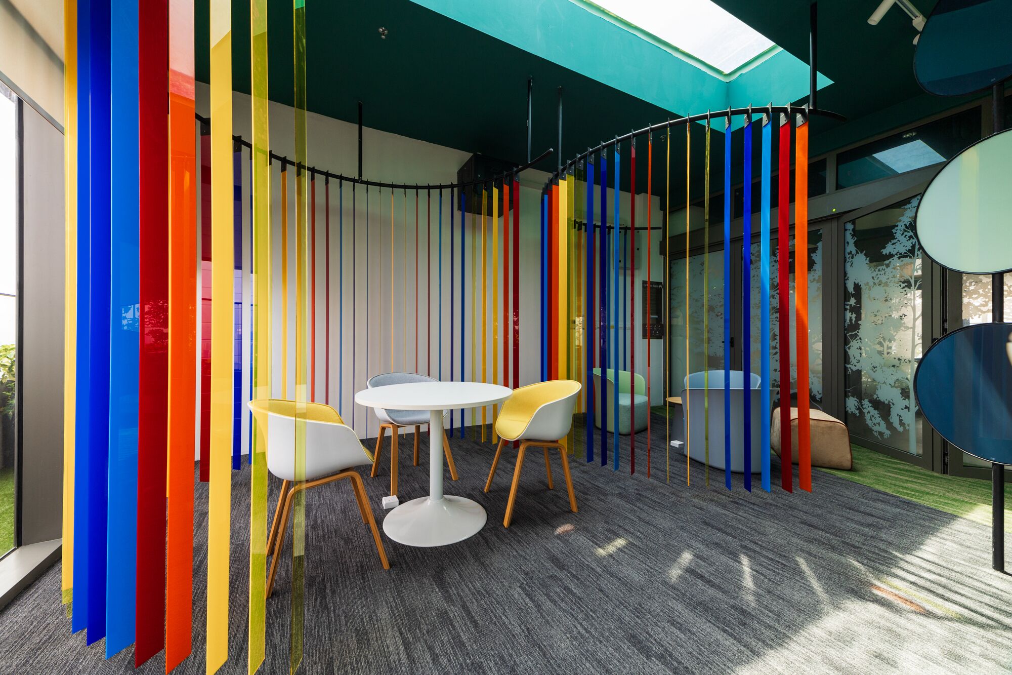 Una sala de reuniones moderna con una mesa redonda, dos sillas y un panel vertical colorido.