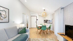 Una sala de estar moderna con un sofá, una mesa de comedor con sillas, un televisor y una zona de cocina al fondo.