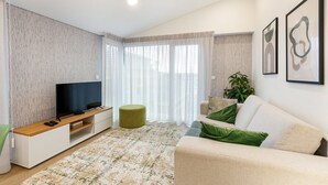 Una sala moderna con una televisión de pantalla plana, un otomán verde, un sofá color beige y obras de arte abstracto en la pared.