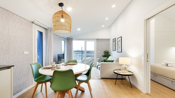 Una sala de estar moderna con comedor, un sofá, una mesita con una lámpara y vista al mar.