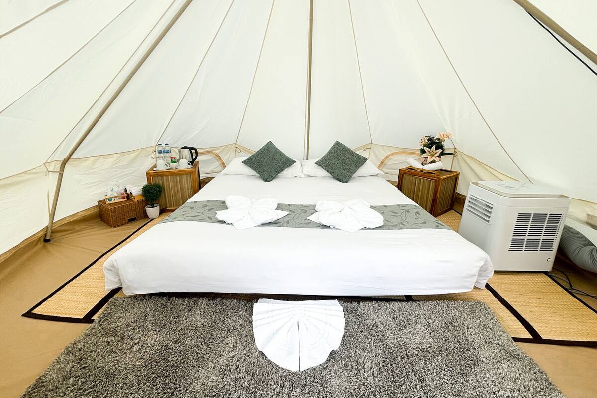 Een tentaccommodatieruimte met een bed, kussens, een nachtkastje, een kachel en een vloerkleed.