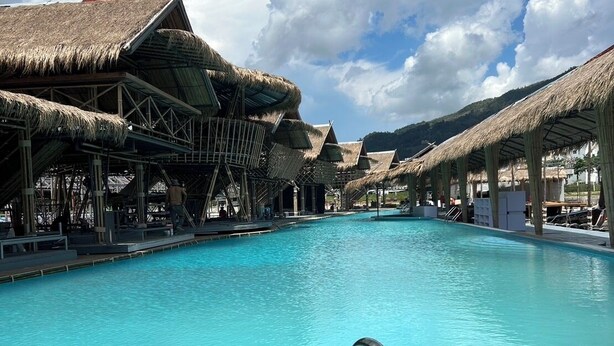 A swimming pool with thatched-roof structures and a clear sky. - Thailand Mountain Phuket (Patong)