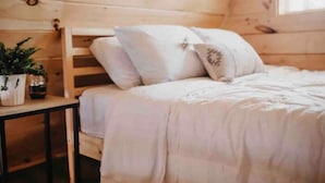 Une chambre confortable dans un chalet en bois, avec un lit, des oreillers et une table de chevet agrémentée d’une plante.