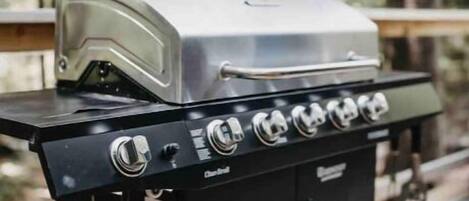 Ein tragbarer Gasgrill mit Deckel und vier Brennern auf einer Holzterrasse.
