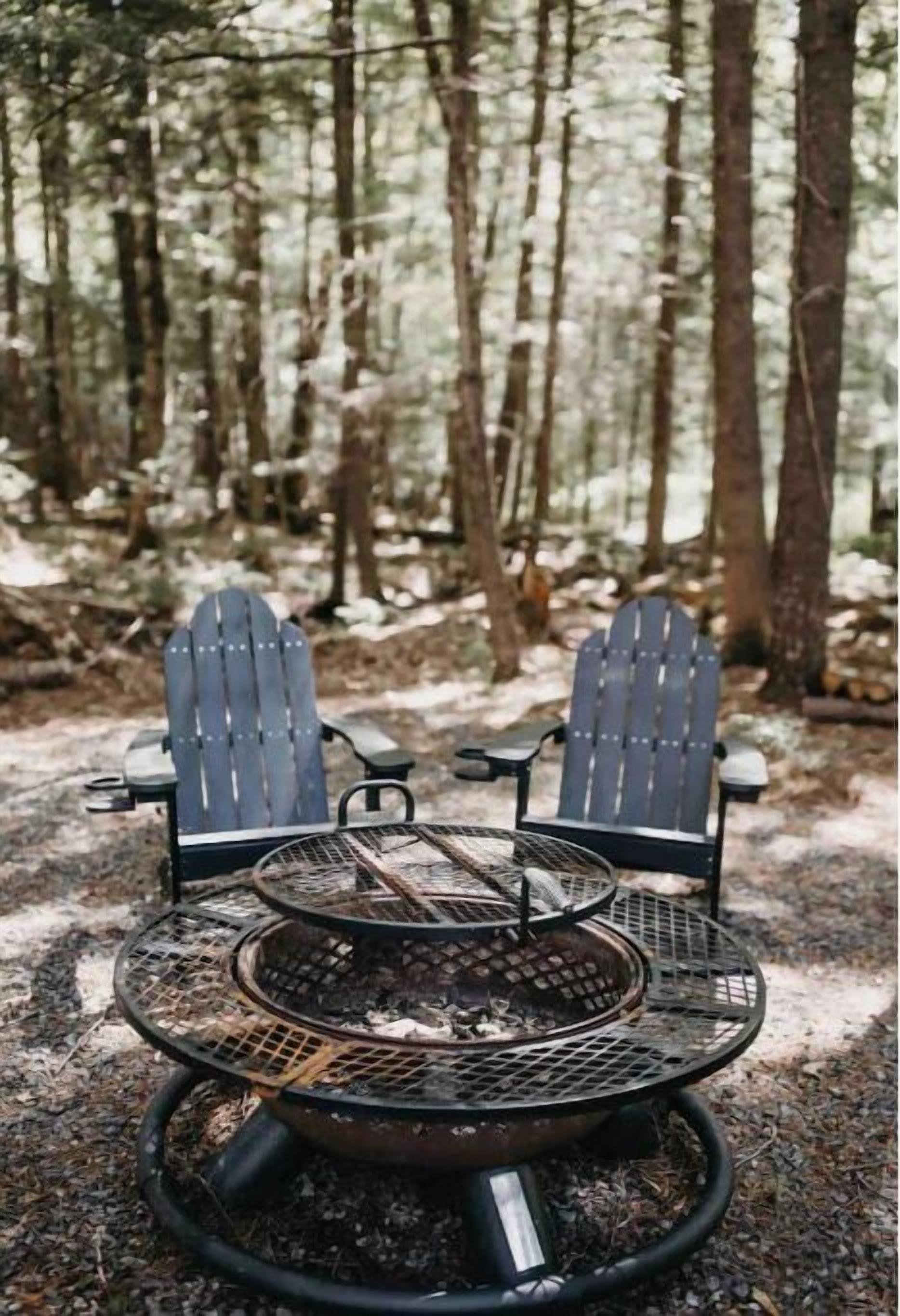 Duas cadeiras Adirondack viradas para uma lareira de metal em um cenário florestal.