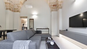 A modern living room with a grey sectional sofa, a coffee table, and a flat-screen TV mounted on the wall.