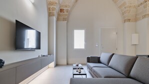 A modern living room with a grey sofa, a flat-screen TV mounted on the wall, and a stone archway.