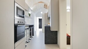 A modern kitchen with a central island, stainless steel appliances, and a high ceiling with exposed brick.