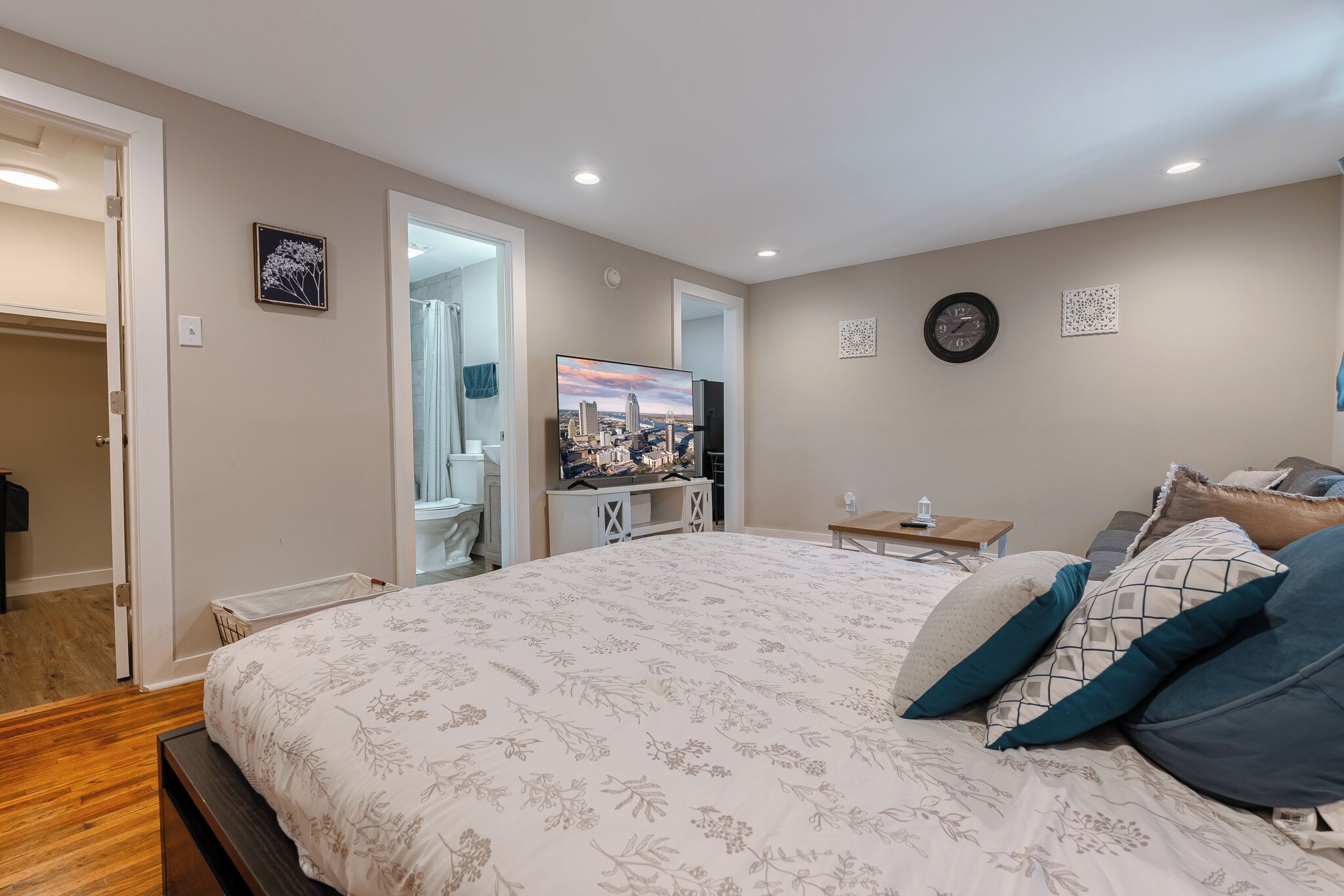 A bedroom with a large bed, a TV on a stand, a bedside table, and a door leading to a bathroom.