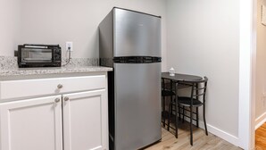 Una cucina funzionale con frigorifero in acciaio inossidabile, forno a microonde integrato, mobili bianchi e un piccolo tavolo con sedie.