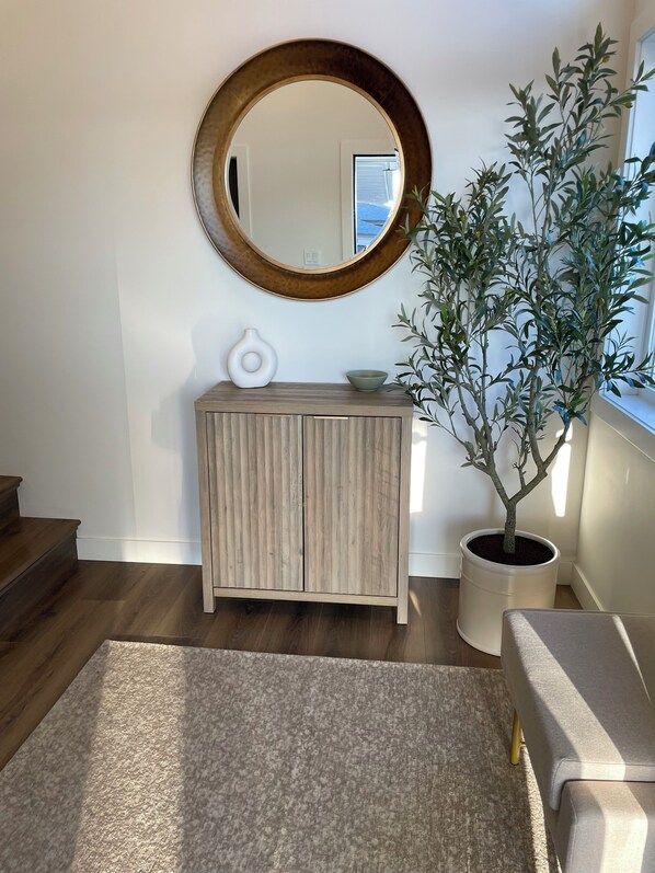 A living room with a wooden cabinet, a round mirror, a potted plant, and a grey sofa.