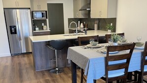 Una cocina moderna con una isla central, electrodomésticos de acero inoxidable y un comedor con mesa dispuesta para cuatro personas.