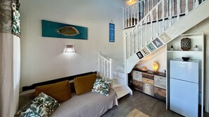 Een ruimtelijk ingerichte leefruimte met een bed, een trap, een keukenhoek en een wandplank.