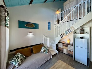 Ein kompakter Wohnraum mit Bett, Treppe, Küchenzeile und Wandregal.