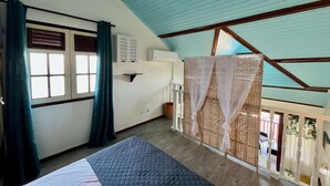 Een kamer met een bed, een raam met gordijnen, een wandairconditioner en een balkon met een rieten afscheiding.
