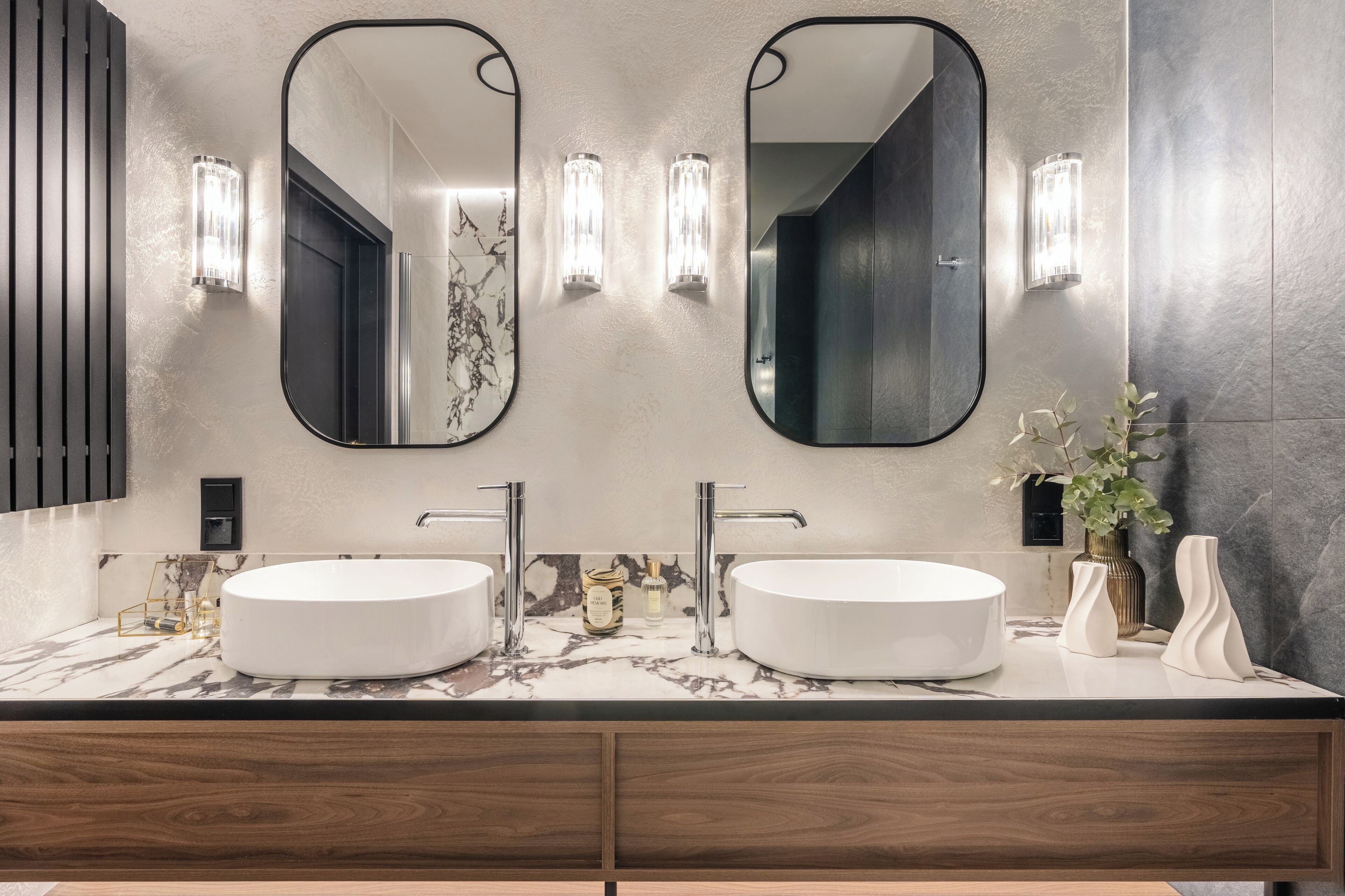 Un baño moderno con dos lavamanos, espejos amplios y apliques de pared.