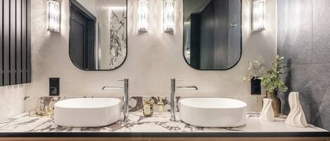 Un baño moderno con dos lavamanos, espejos amplios y apliques de pared.