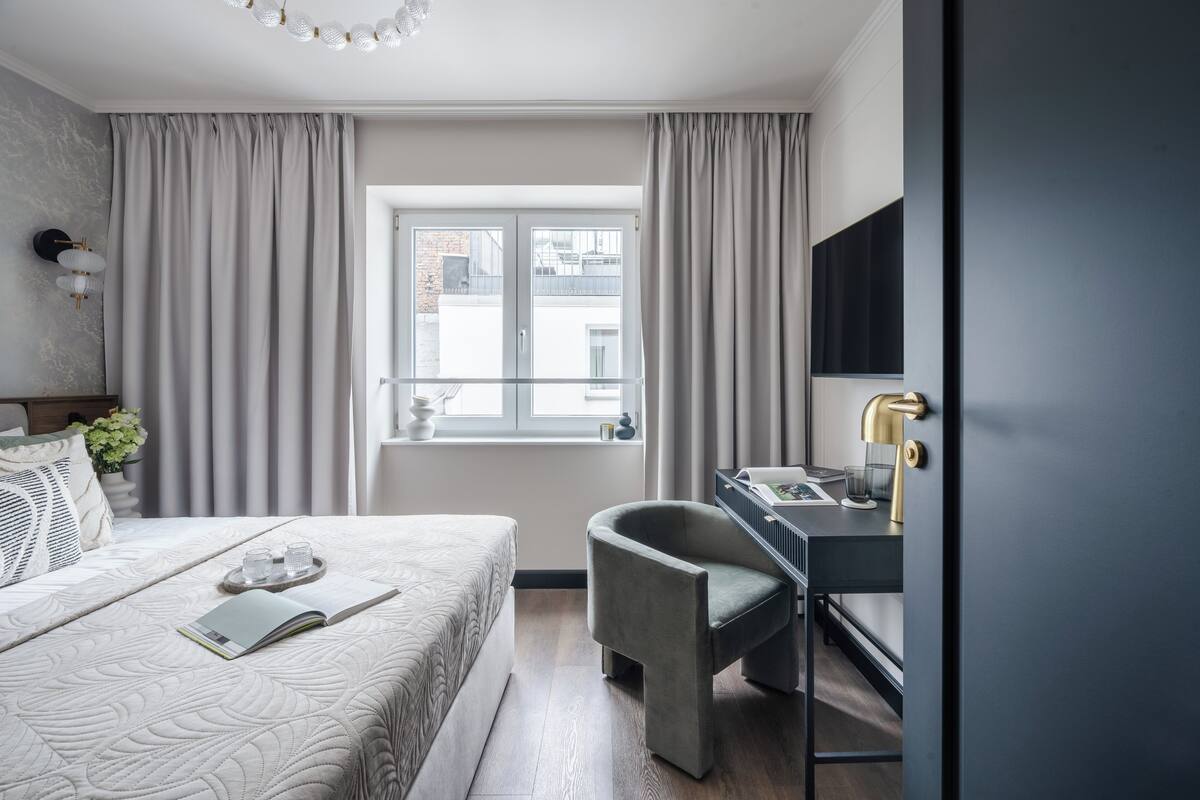 Une chambre d’hôtel moderne équipée d’un lit, d’un bureau, d’une chaise et d’une fenêtre avec des rideaux.