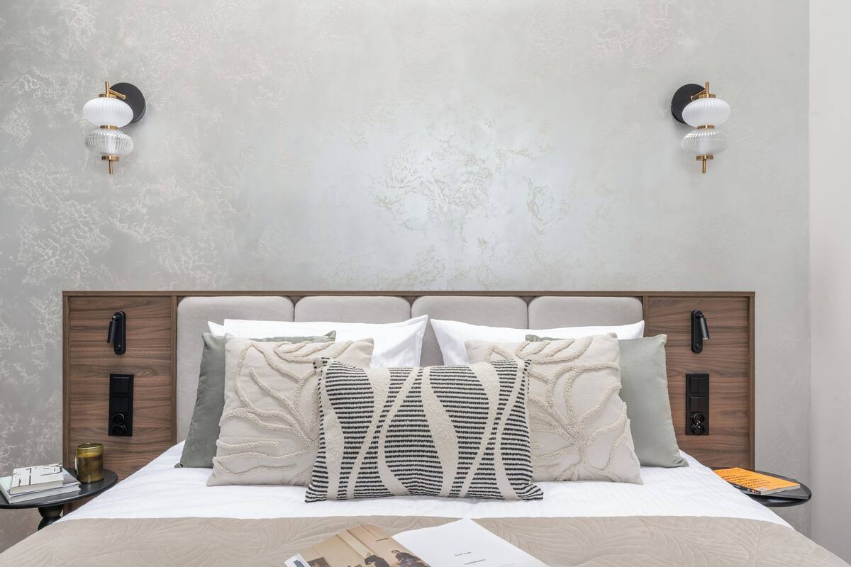 Un lit bien fait, avec une tête de lit en bois, deux tables de chevet et des lampes fixées au mur.