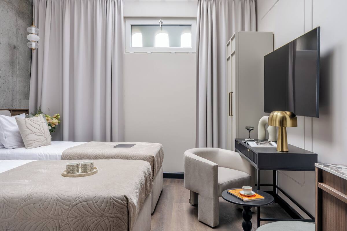 Une chambre d’hôtel avec deux lits, un bureau avec une chaise, une télévision et une fenêtre avec des rideaux.