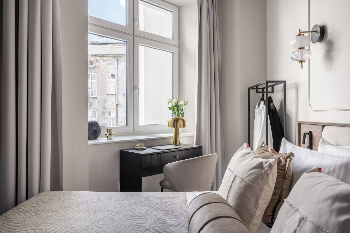 Une chambre d’hôtel moderne avec un grand lit, un bureau avec une lampe, une vue sur la ville par la fenêtre et une armoire.