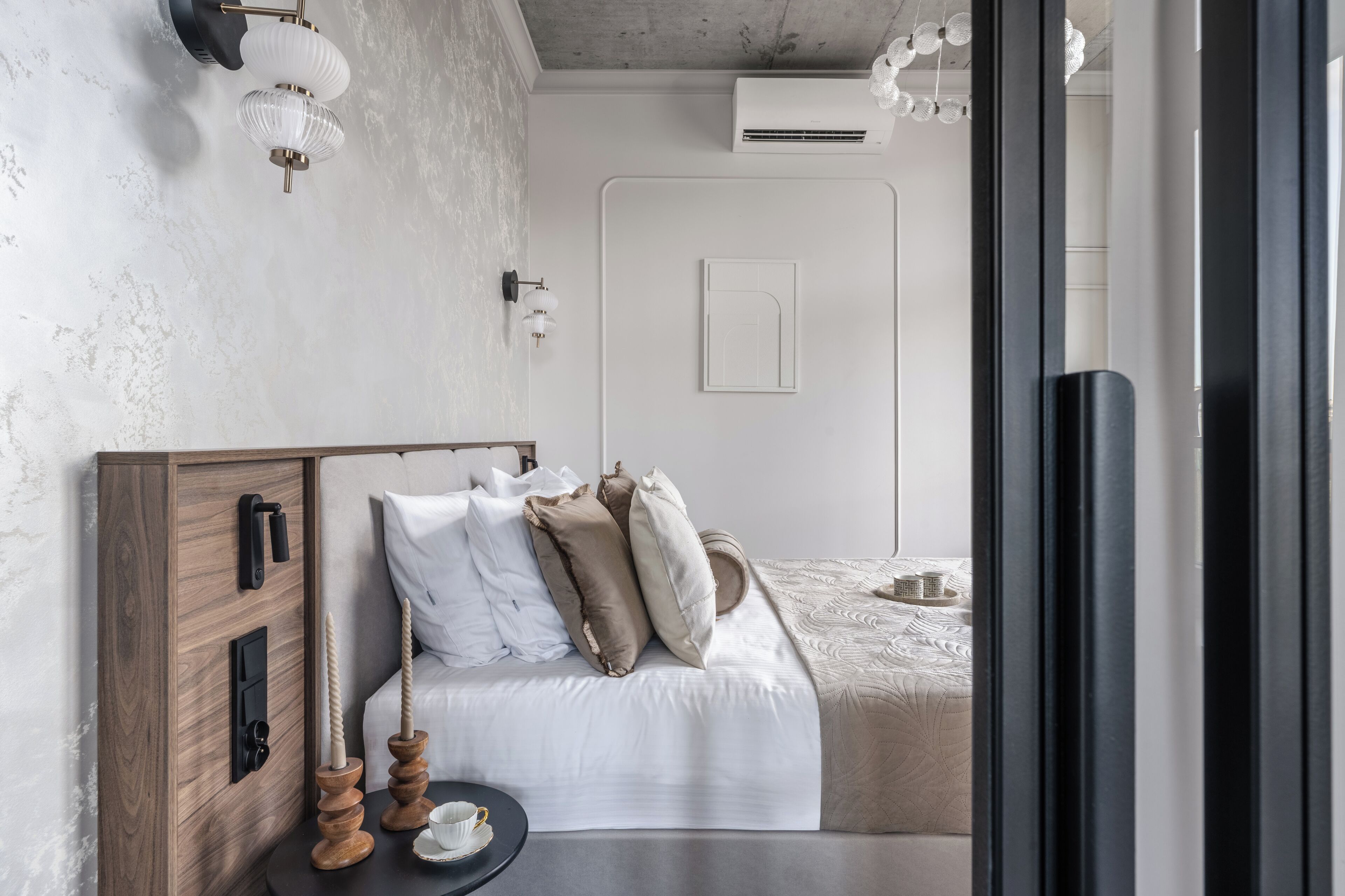 Ein Schlafzimmer mit Holz-Kopfteil, einem Bett mit weißer und beiger Bettwäsche, einem Nachttisch mit Kerzen und einer wandmontierten Leuchte.