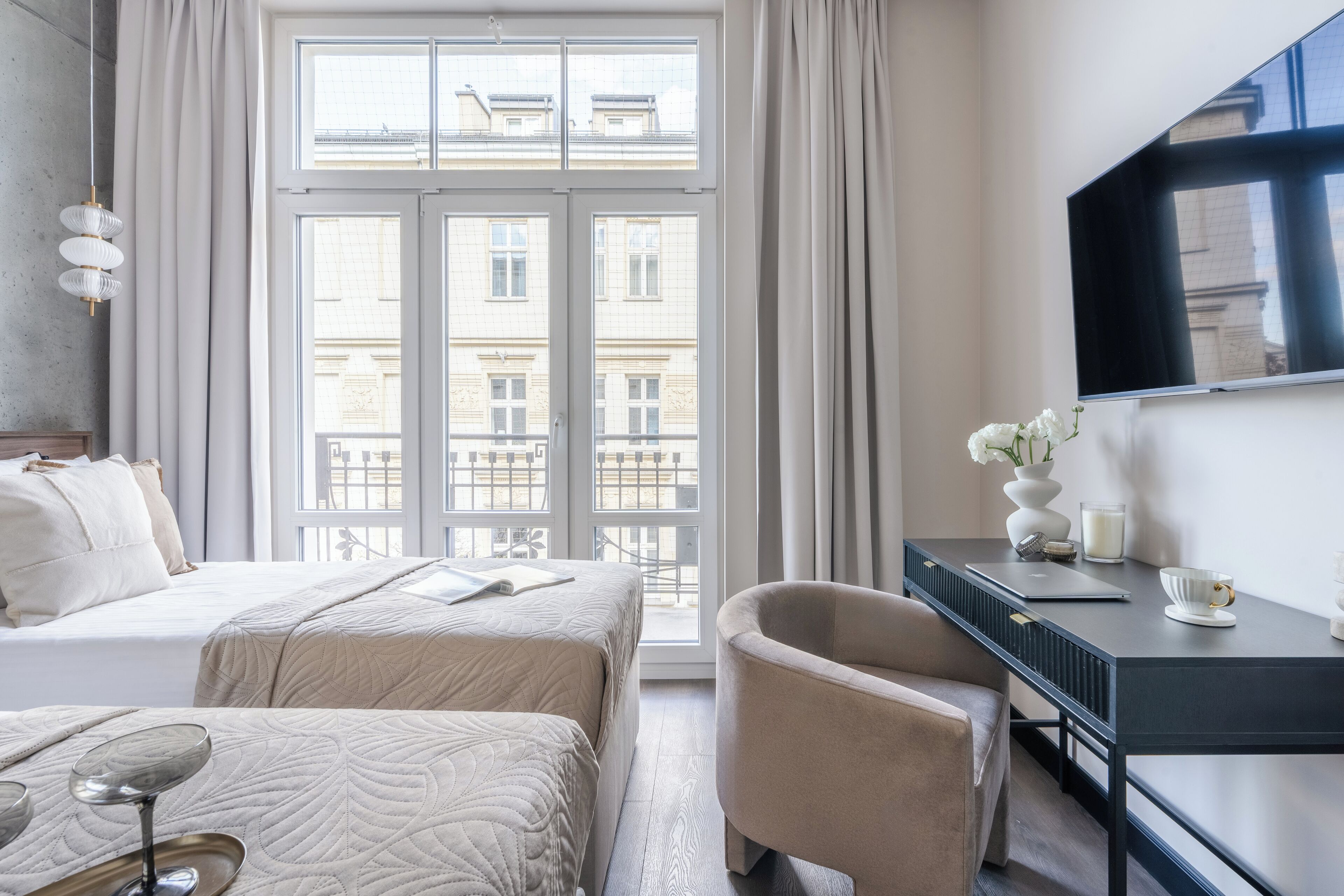 Une chambre d’hôtel équipée d’un lit, d’un bureau, d’une chaise, d’une télévision et d’une fenêtre donnant sur des immeubles.