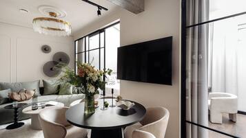 Una sala de estar moderna con una mesa de comedor redonda, asientos cómodos, un ventanal grande y un televisor montado.