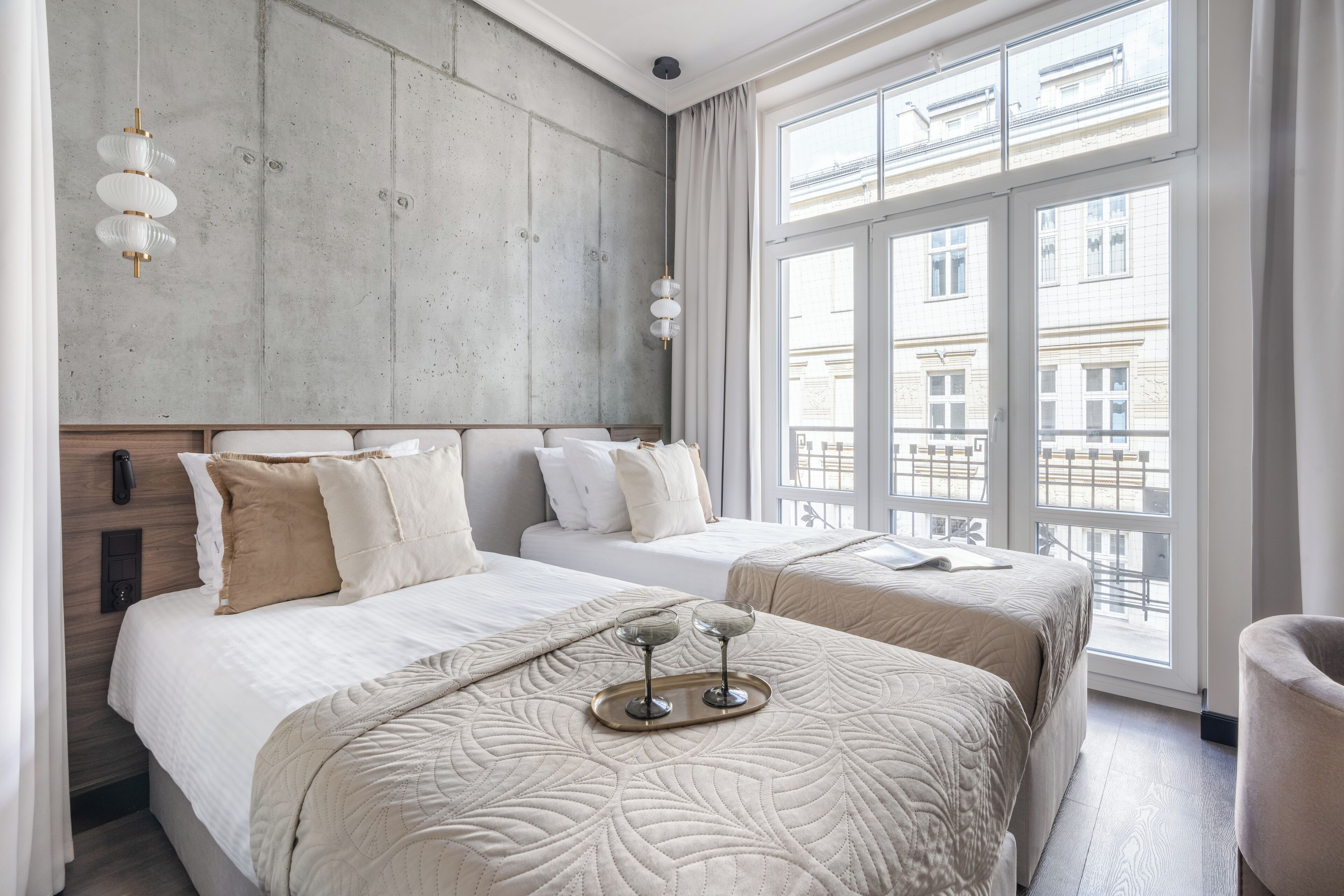 A hotel room with two beds, a large window, and a tray with two glasses on the bed.