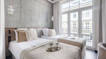 A hotel room with two beds, a large window, and a tray with two glasses on the bed.