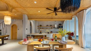 A dining area with a wooden table set for four, surrounded by chairs with blue cushions. A ceiling fan and pendant light are visible above. - Panorama Paddy Retreat - Luxury Villa & Pool (Thành phố Hội An)