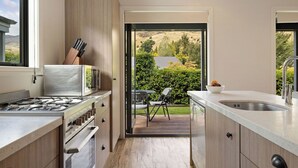A modern kitchen with a gas stove, stainless steel appliances, and a view of a landscaped garden through an open door. - Cardrona Retreat, Resort spa & swimming pool (Cardrona)