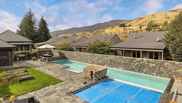 A pool area with stone walls, a stone deck, and a grassy lawn with lounge chairs. - Cardrona Retreat, Resort spa & swimming pool (Cardrona)
