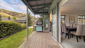 A covered outdoor area with a barbecue, dining table, and chairs, overlooking a hillside. - Cardrona Retreat, Resort spa & swimming pool (Cardrona)