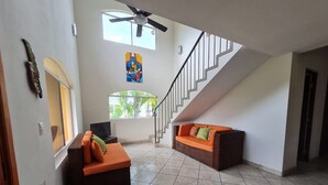 A spacious living area with a staircase, two sofas with cushions, a ceiling fan, and a large window.