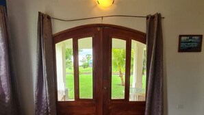 A room with a wooden door leading outside, a bed with white bedding, and a small table.