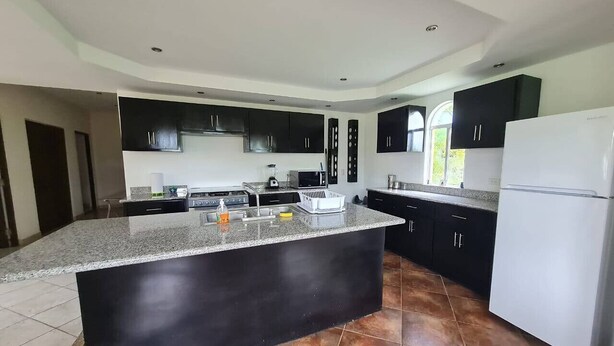 A modern kitchen with black cabinets, a granite countertop, and a white refrigerator.