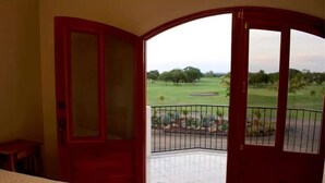 A room with a bed, a red door, and a balcony with a view of a golf course.