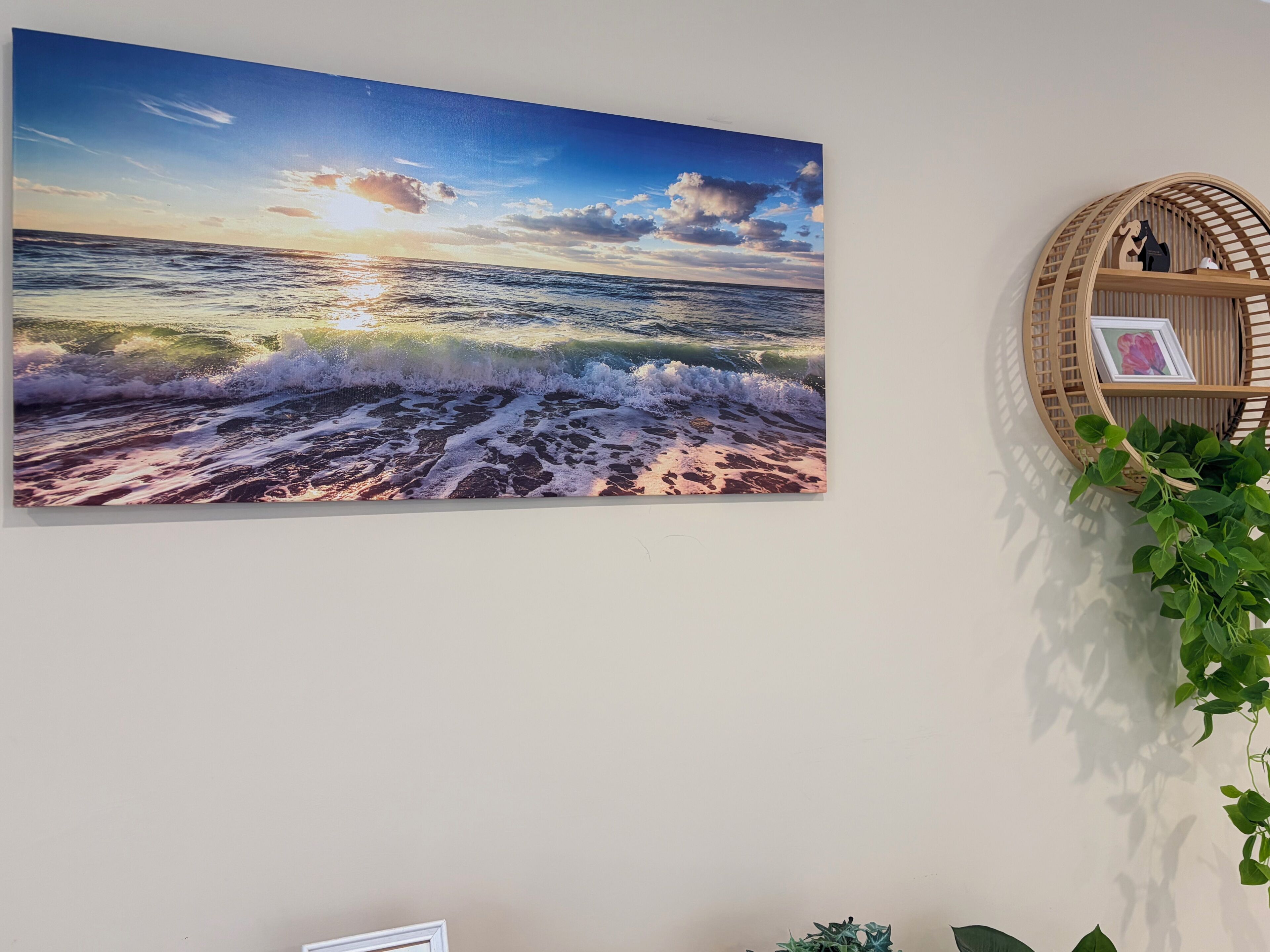 A wall-mounted painting of a beach scene with waves and a sunset.